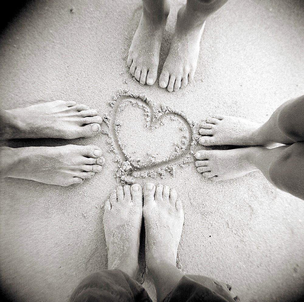 Image taken with a Holga medium format 120 film toy camera of four pairs of feet standing around a heart shape drawn in sandy beach, Taransay, Outer Hebrides, Scotand, United Kingdom, Europe