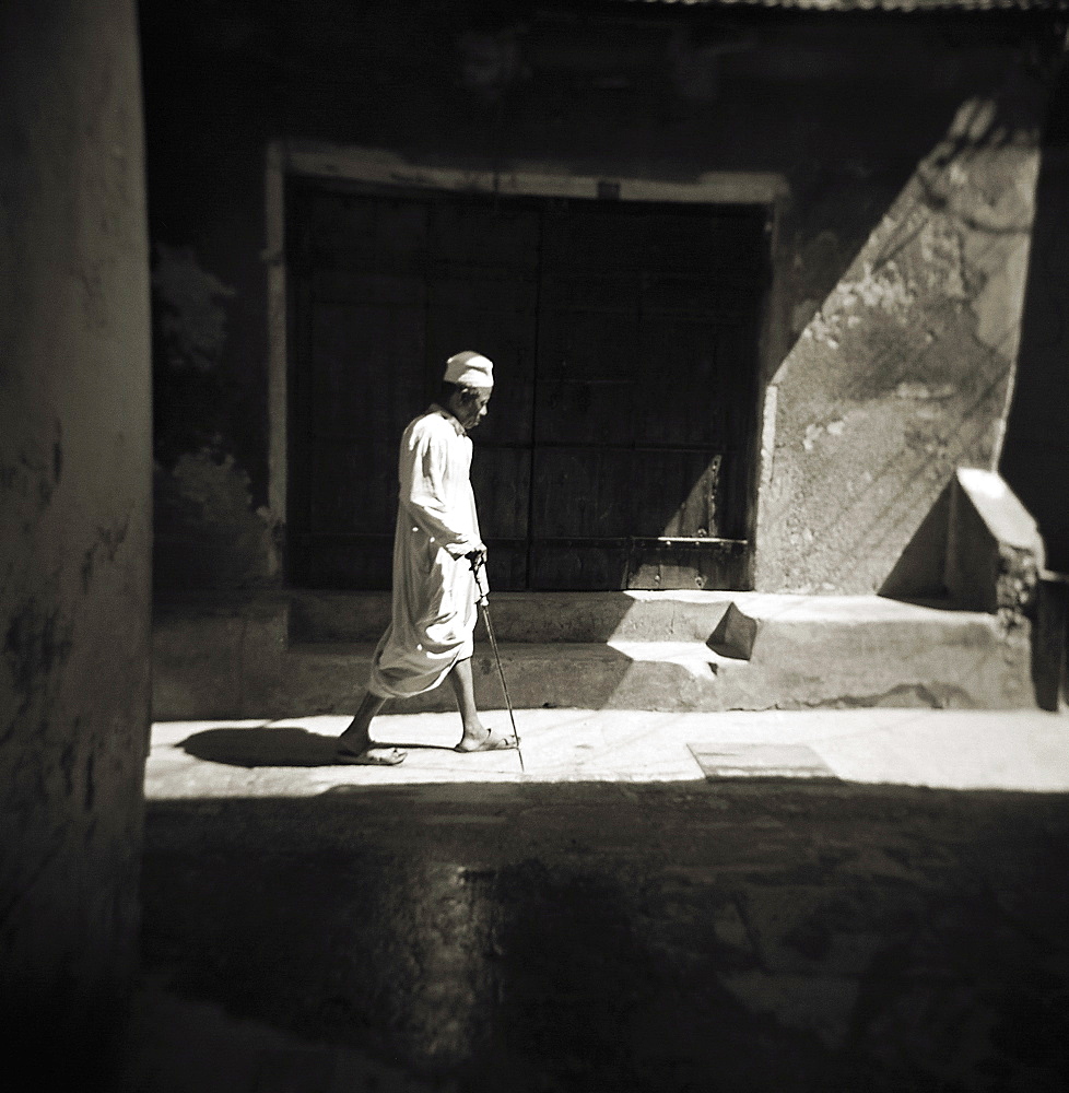 Image taken with a Holga medium format 120 film toy camera of a man in white djellaba caught in sunlight in backstreets of Stonetown, Zanzibar, Tanzania, East Africa, Africa