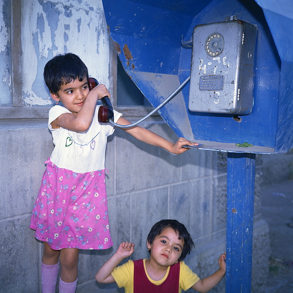 Two small Uzbek girls using the public telephone in Bukhara, Uzbekistan, Central Asia, Asia