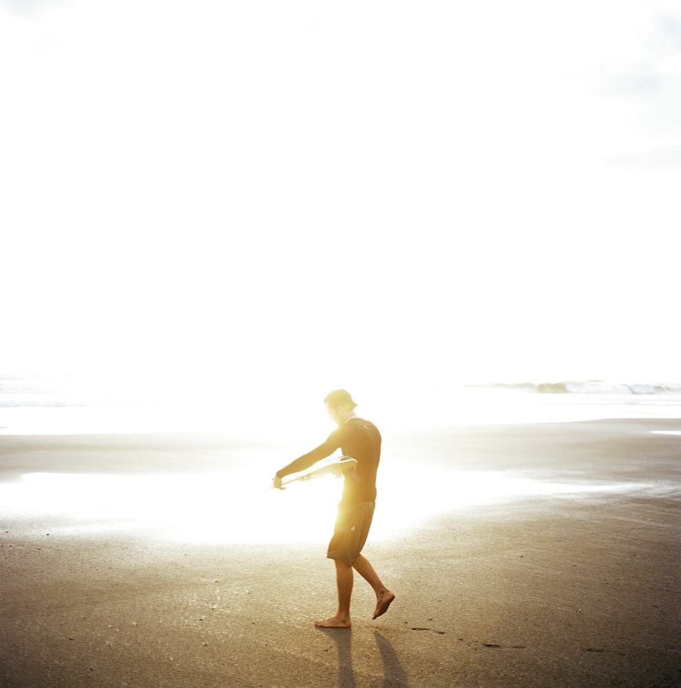 Young man waxes his board before entering Marabella's waves, Costa Rica, Central America