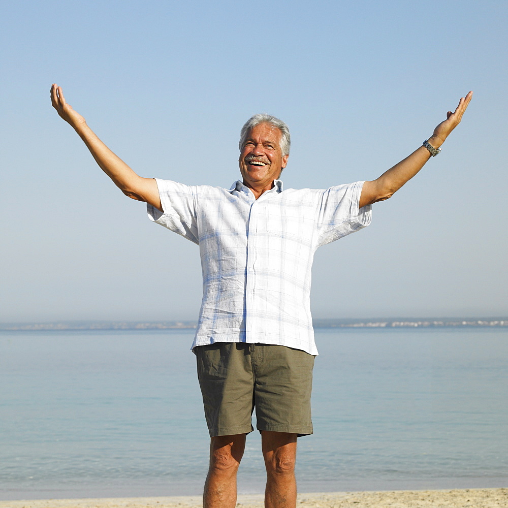 Senior man on beach with arms raised