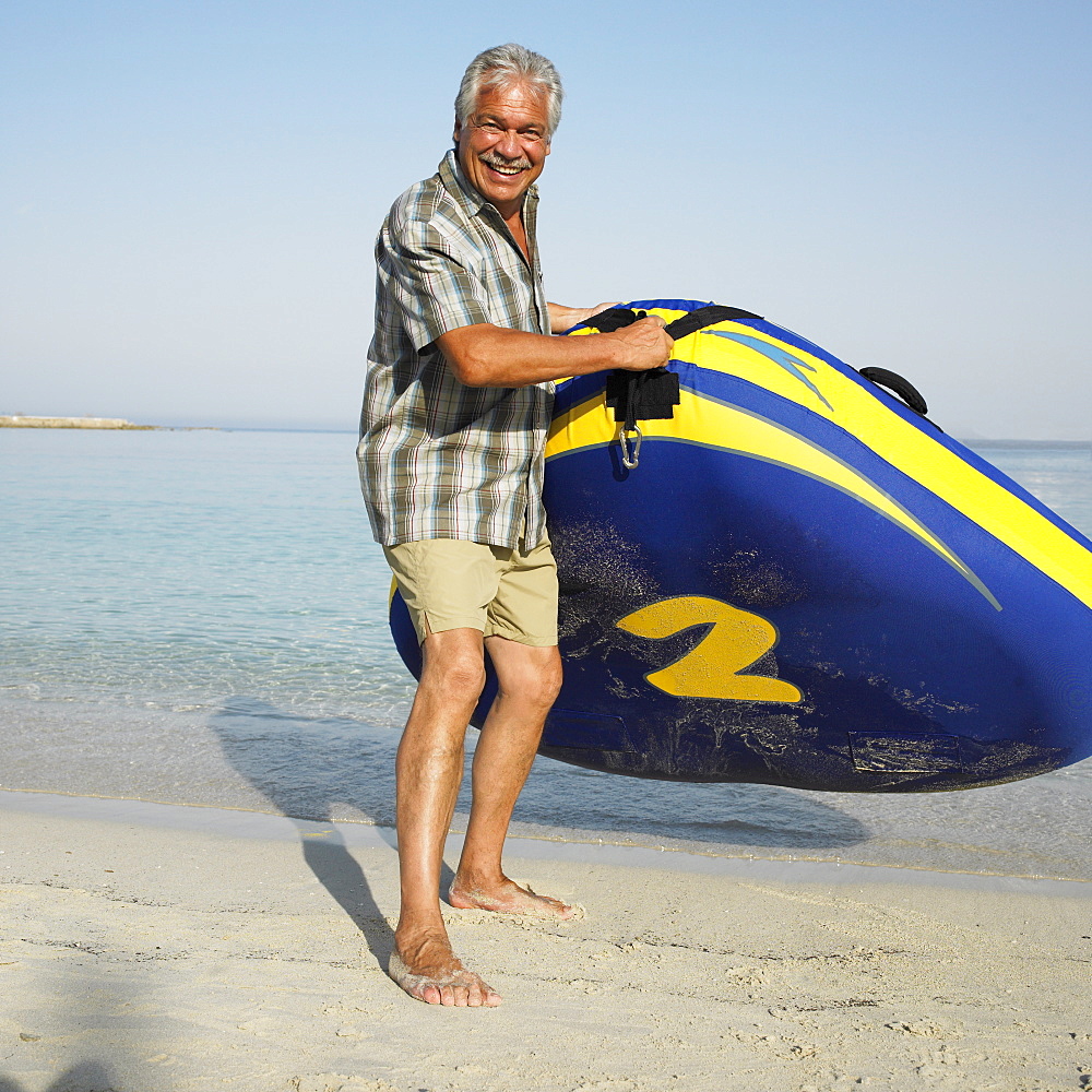 Senior man on beach with inflatable dinghy