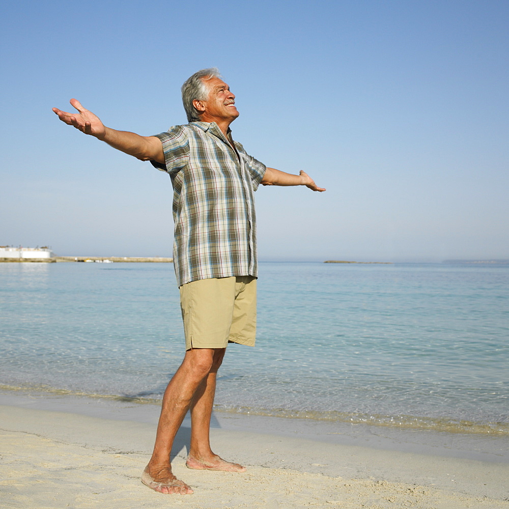 Happy senior man on beach with arms raised