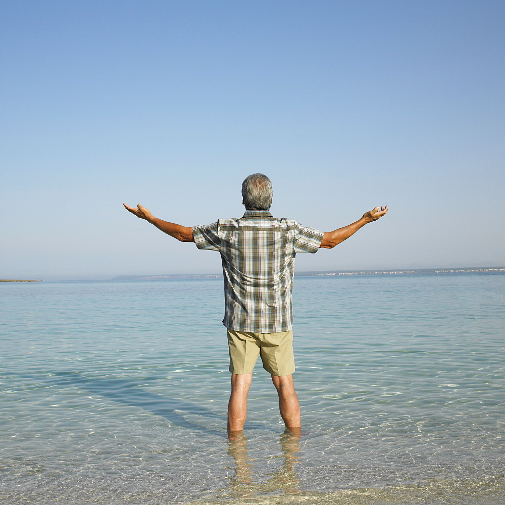 Happy senior man on beach with arms raised