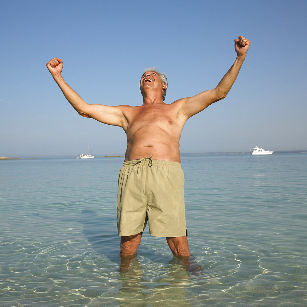 Happy senior man on beach with arms raised