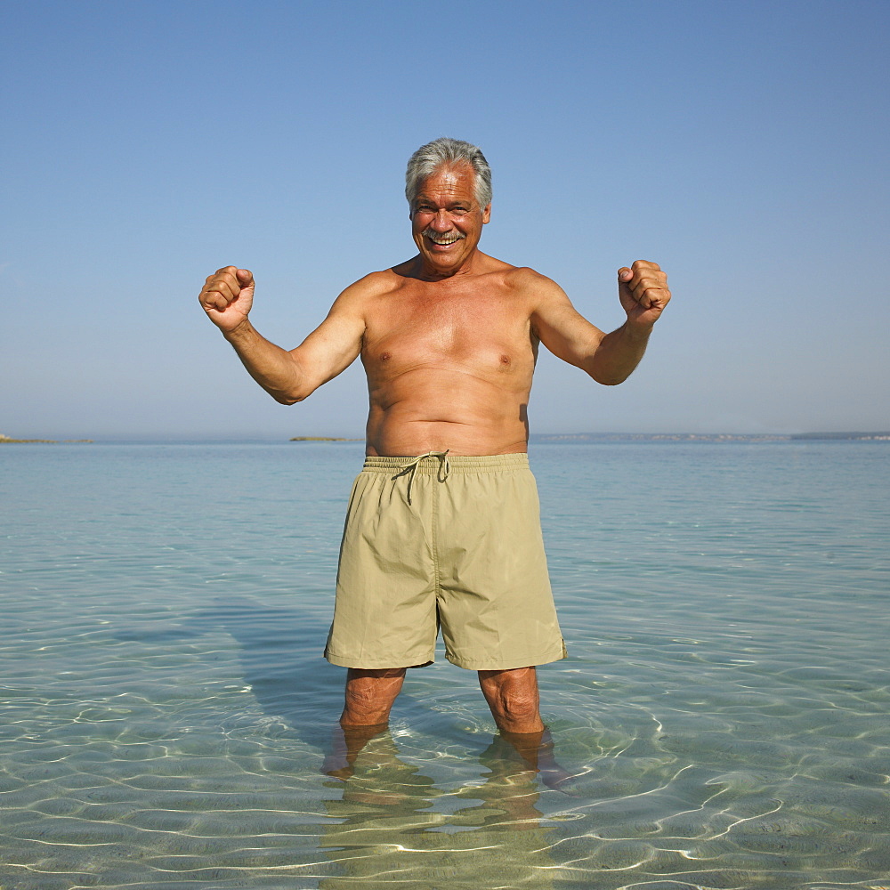 Happy senior man on beach with arms raised