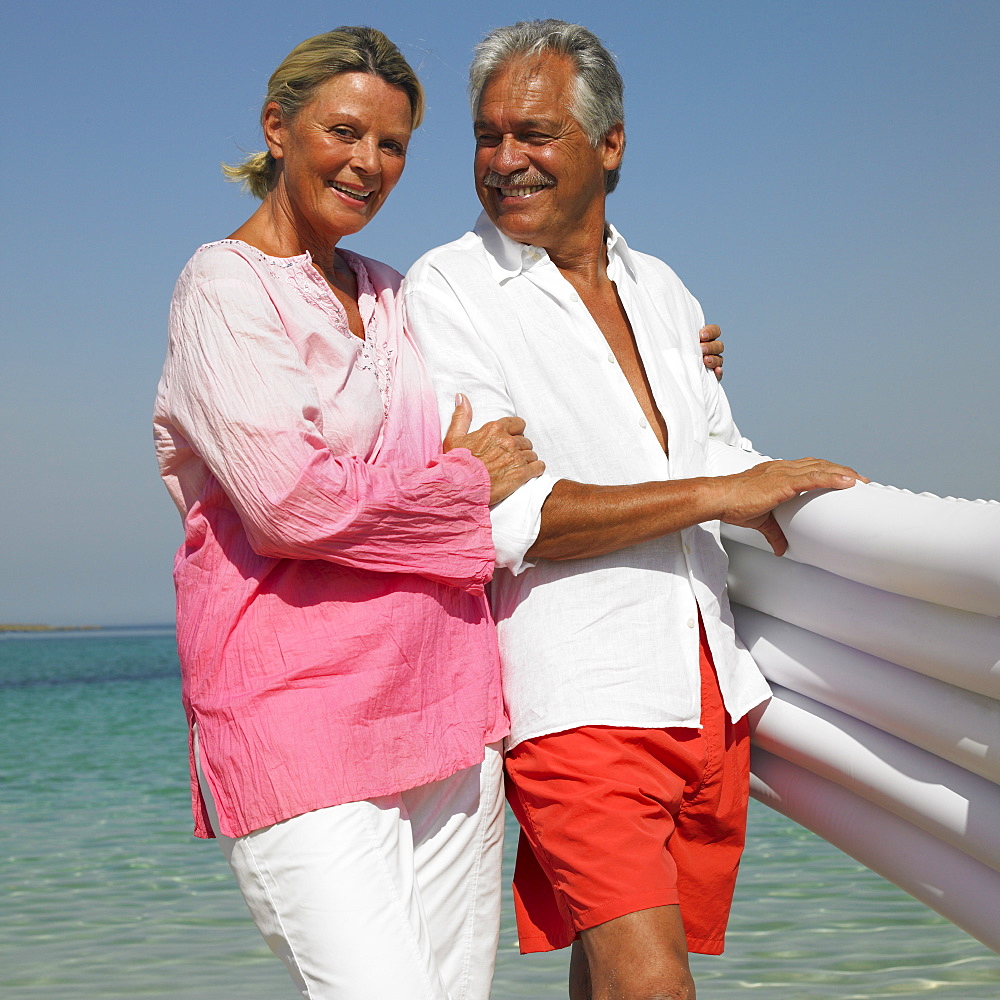 senior couple on beach holding air bed