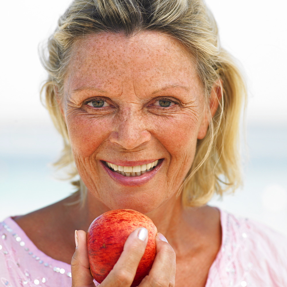 senior woman on beach holding apple, close-up