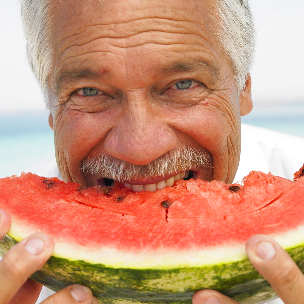 Senior man on beach eating water melon