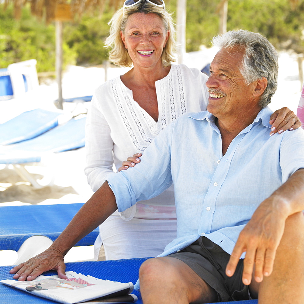 senior couple on beach on sunloungers