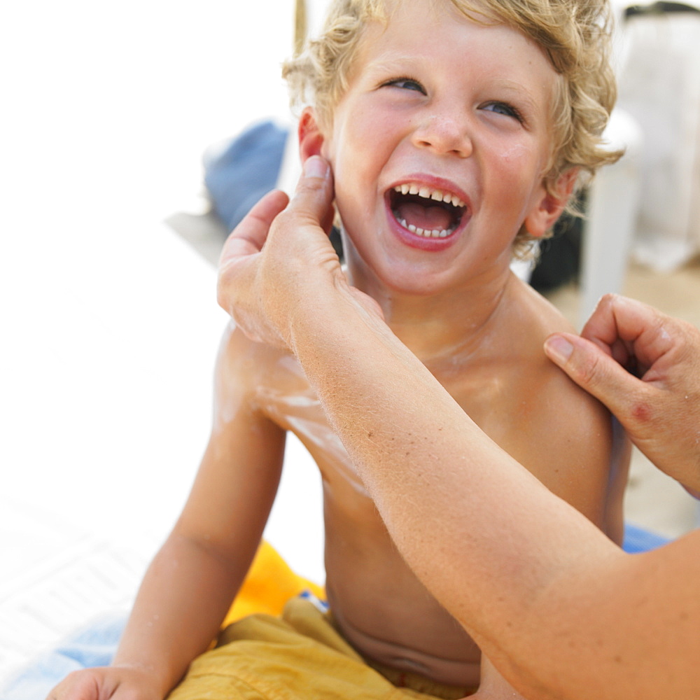 Boy (6-8) on beach having suncream applied