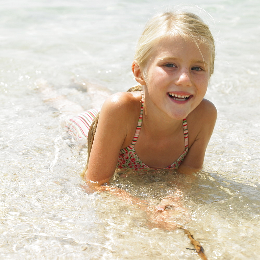 Girl (6-8) on beach lying in the surf