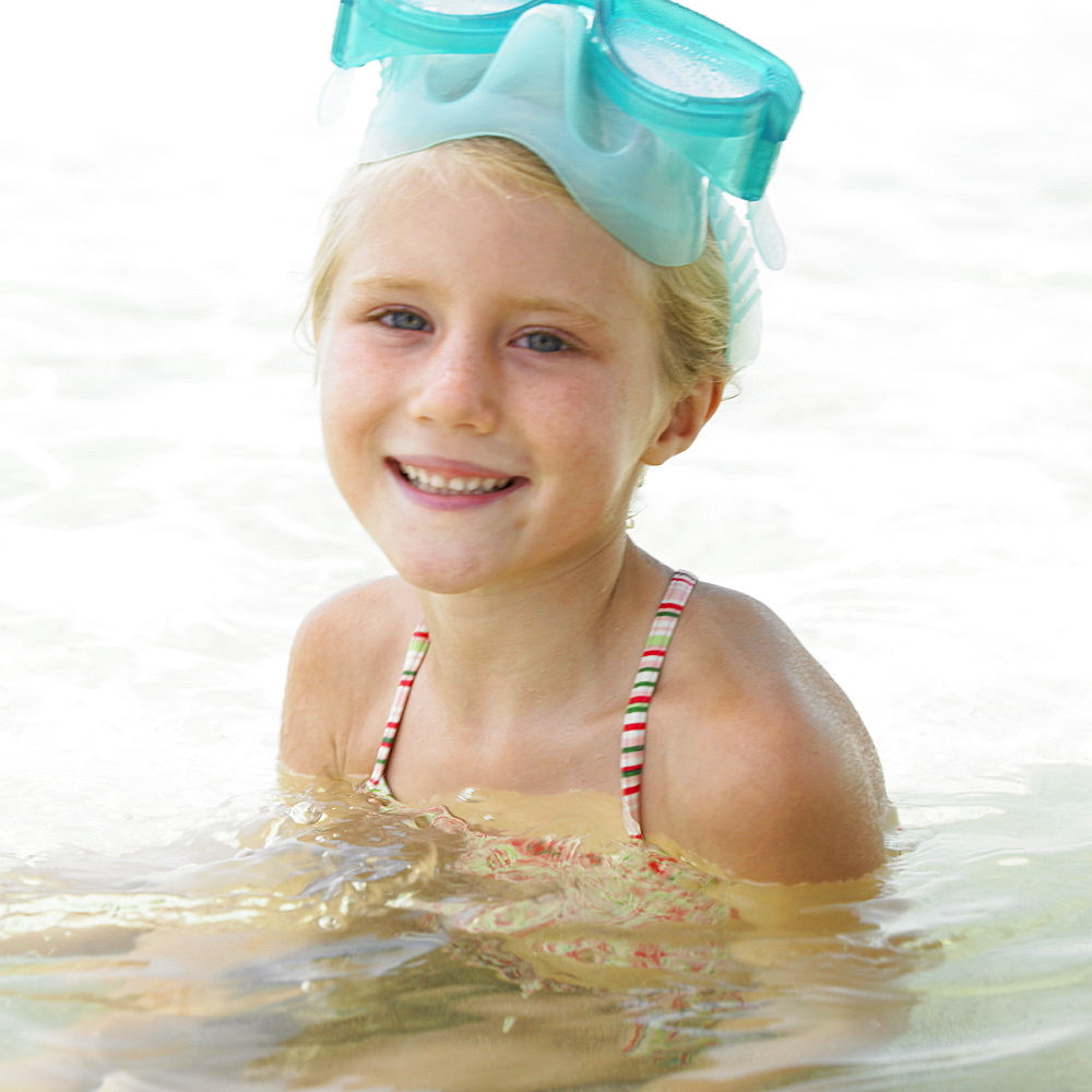 Girl (6-8) wearing swimming goggles in the surf