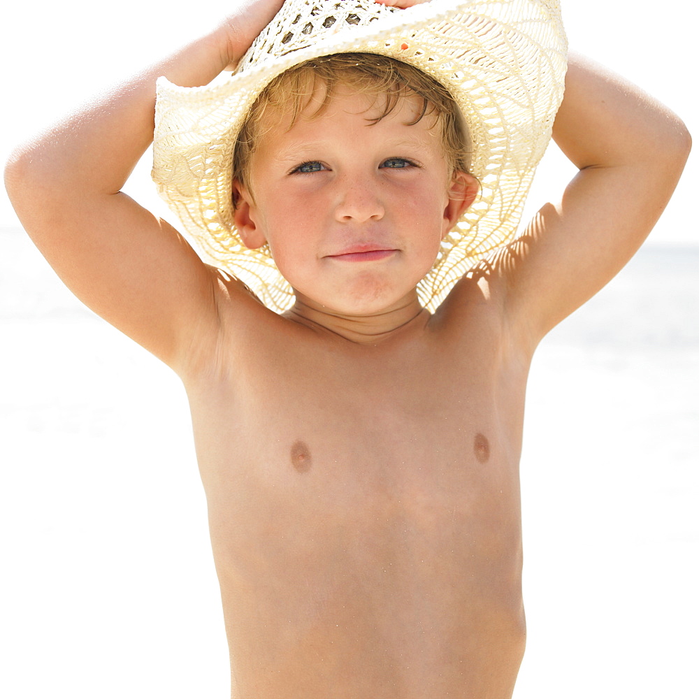 Boy (6-8) on beach wearing straw hat