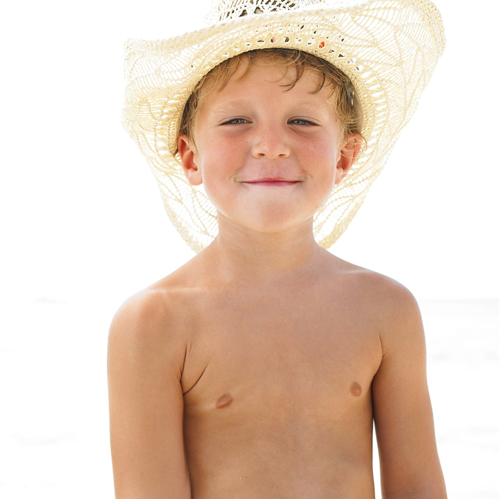 Boy (6-8) on beach wearing straw hat