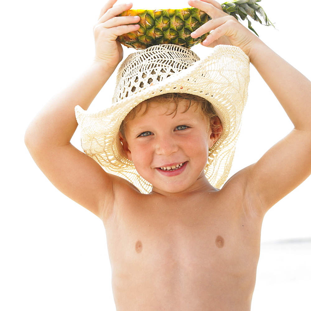 Boy (6-8) on beach holding slice of pineapple