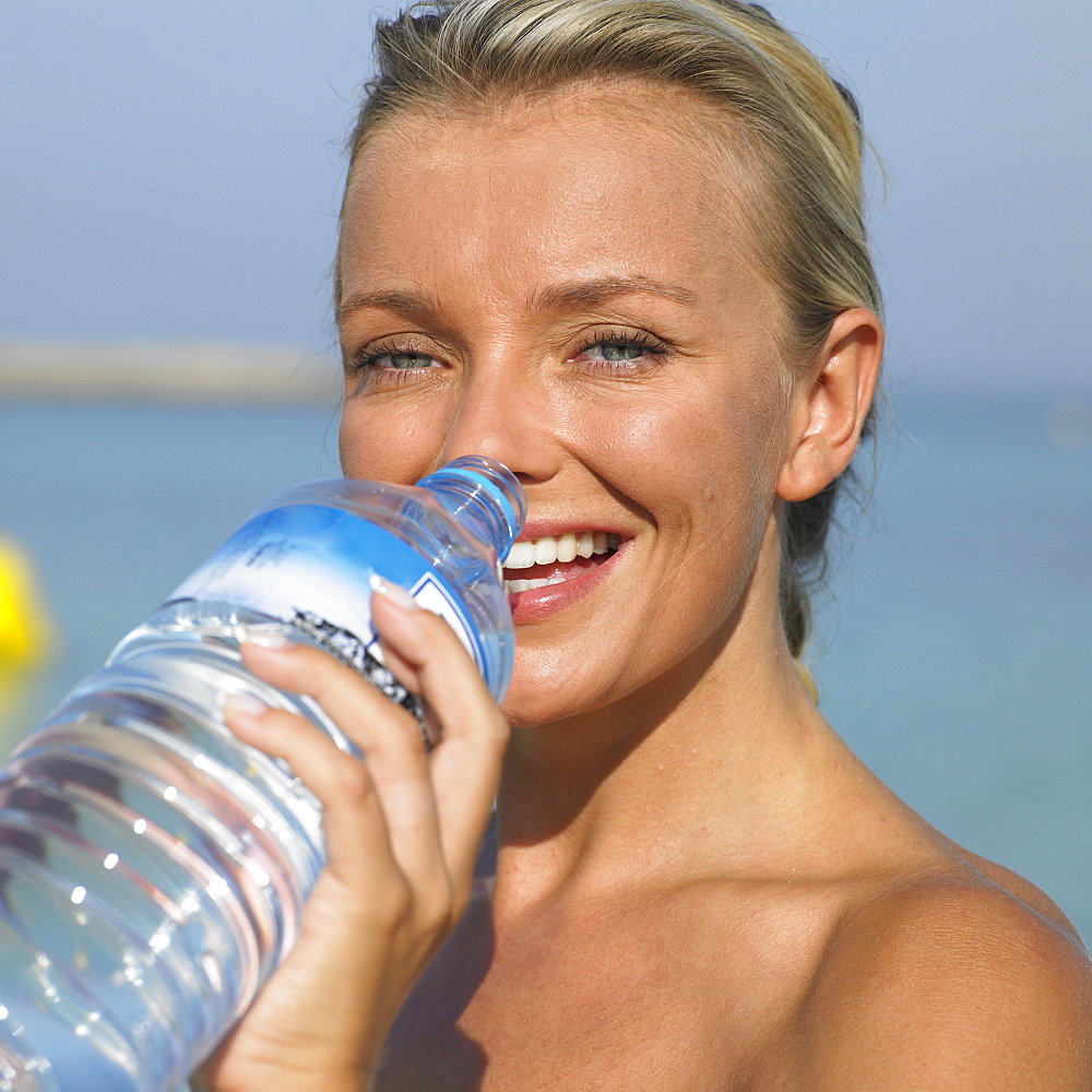 Woman drinking from water bottle on beach, close-up