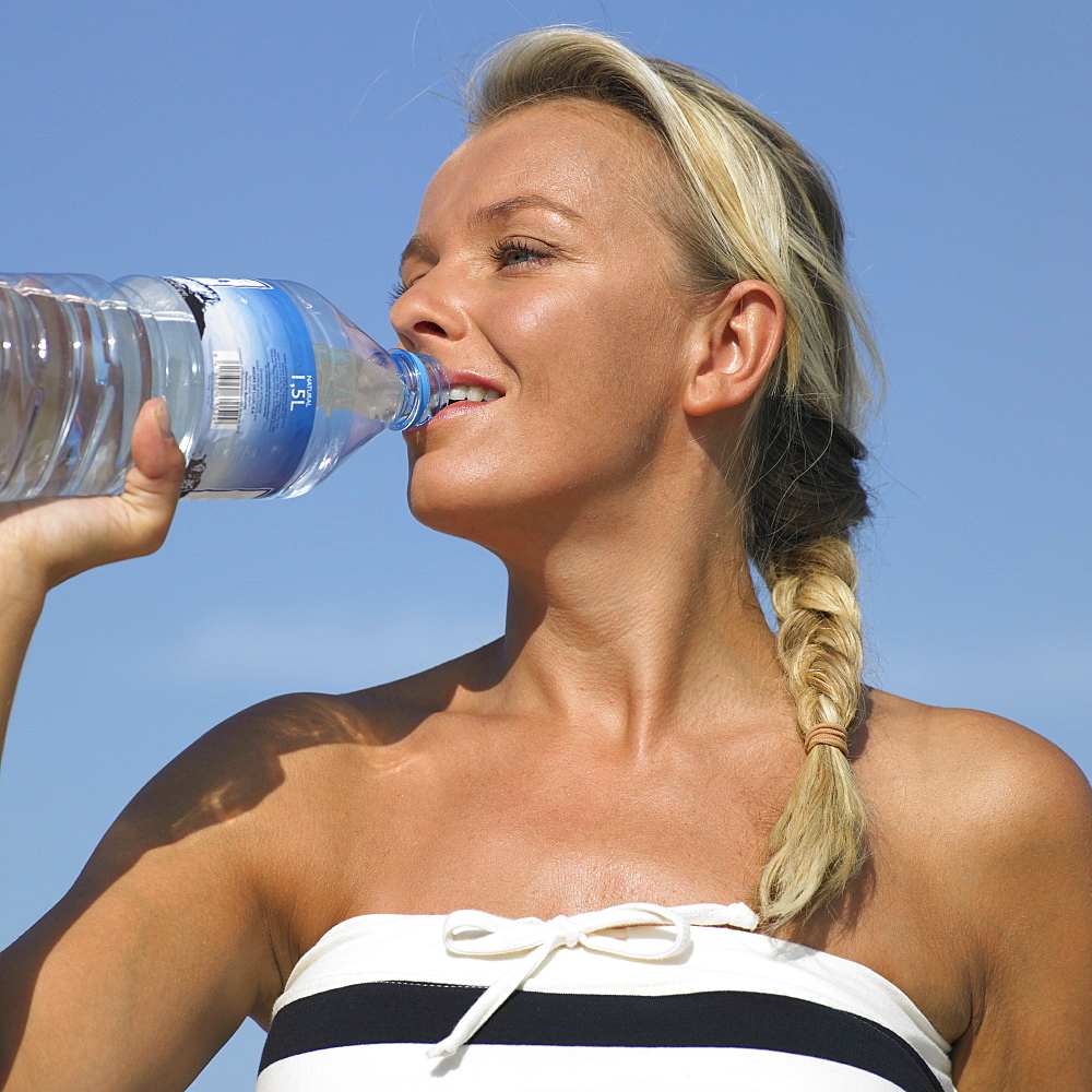 Woman drinking from water bottle on beach, close-up