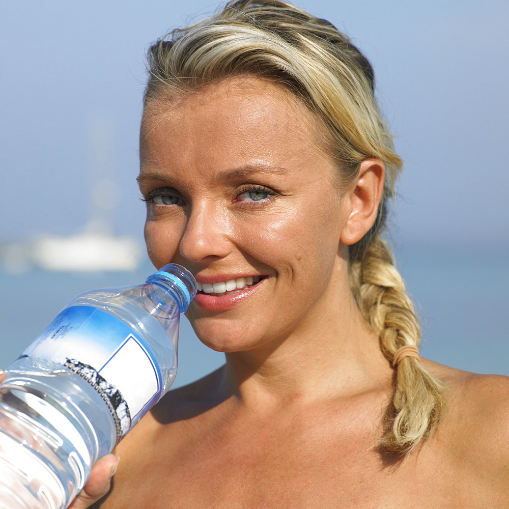 Woman drinking from water bottle on beach, close-up