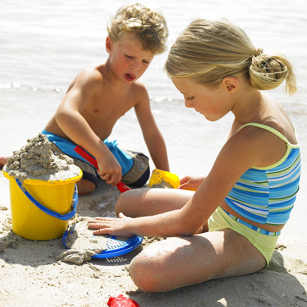 Boy and girl (6-8) on beach making sandcastles