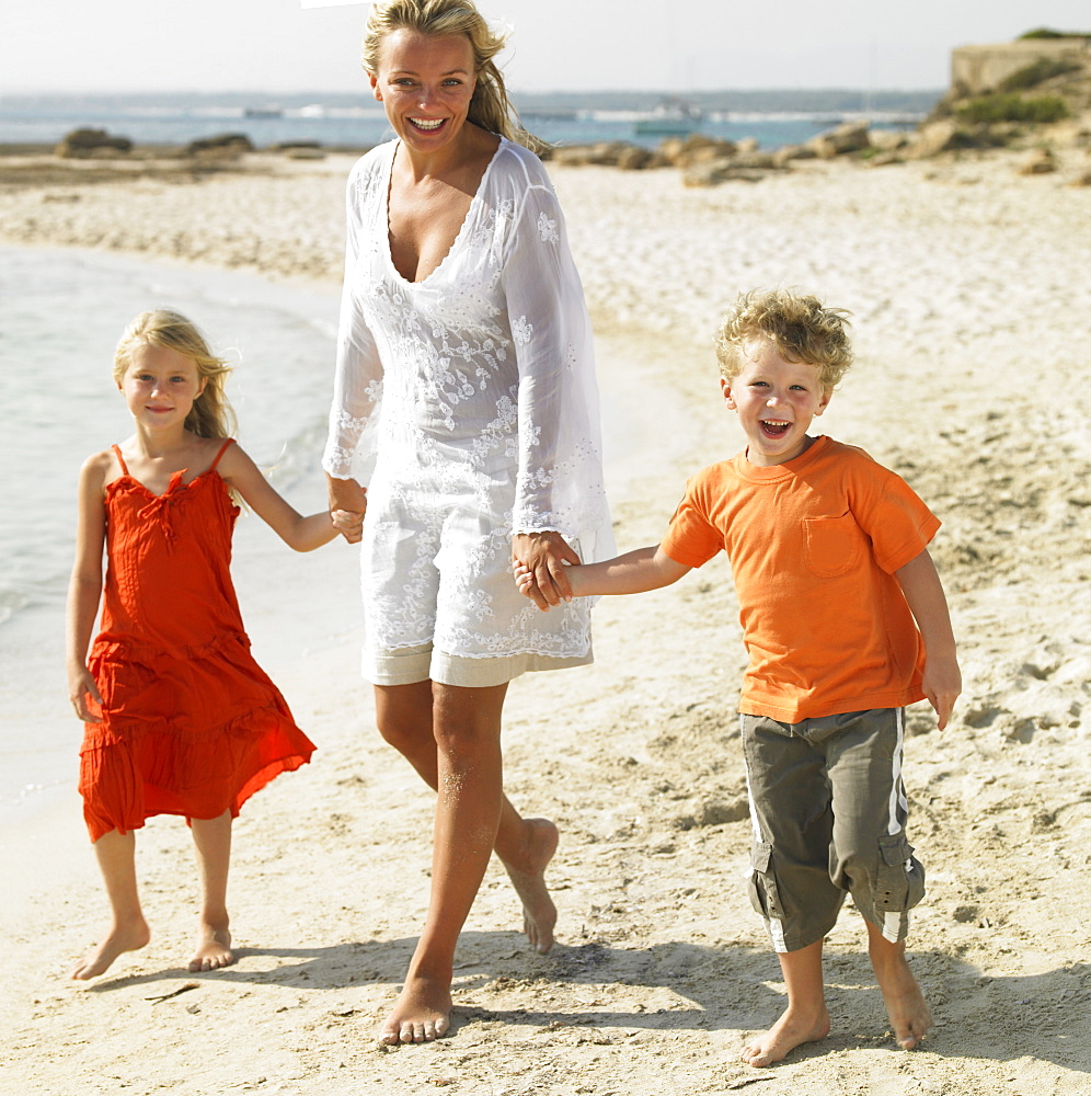 Mother and children (6-8) walking on beach