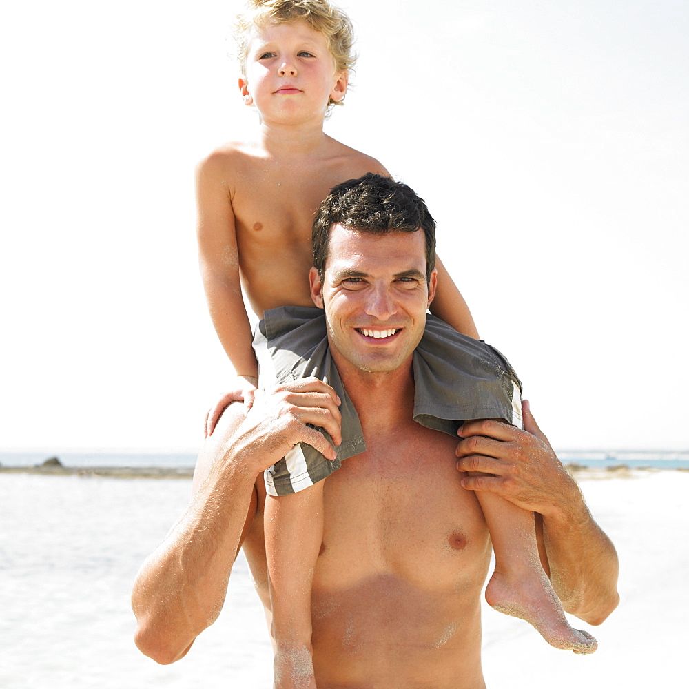 Son (6-8) sitting on father's shoulders on beach