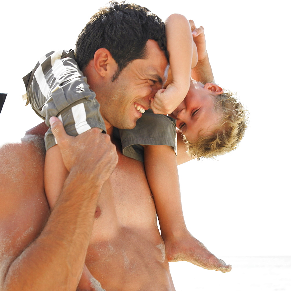 Son (6-8) sitting on father's shoulders on beach