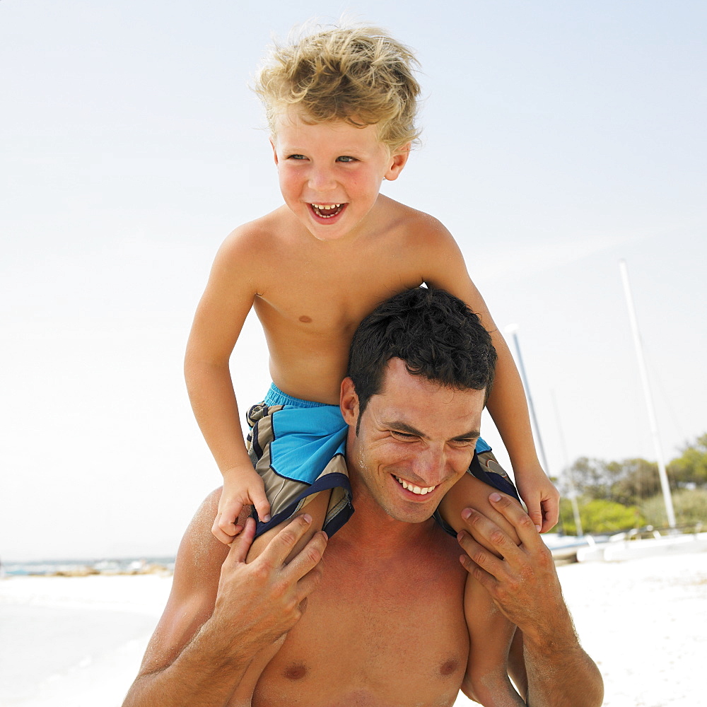 Son (6-8) sitting on father's shoulders on beach