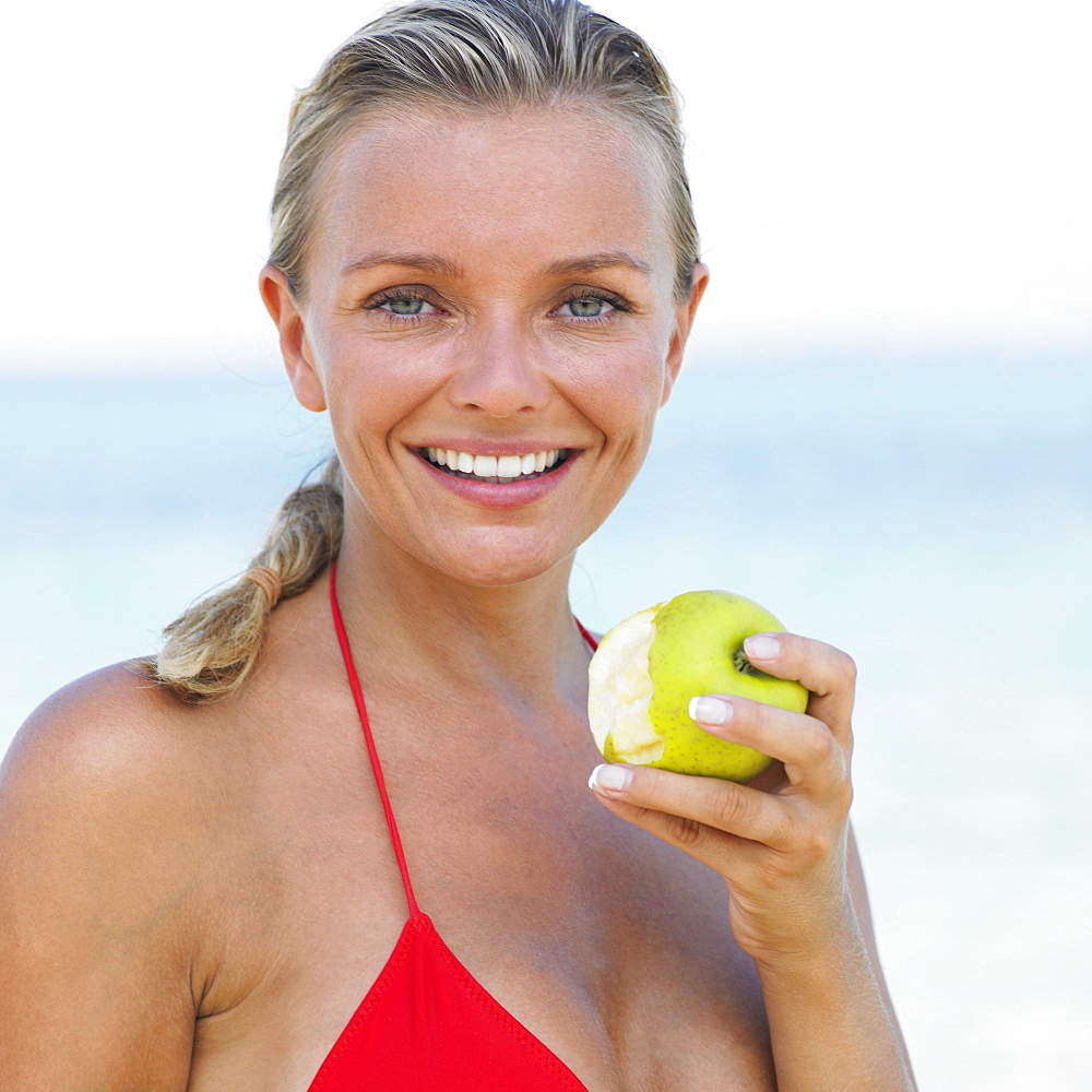 Woman in bikini on beach holding apple