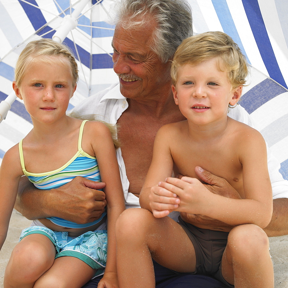 Grandfather and grandchildren (6-8) under parasol