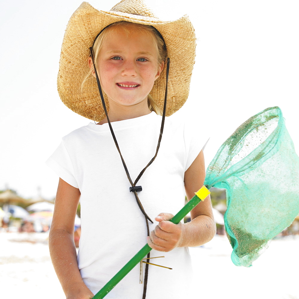 Girl (6-8) on beach wearing straw hat, carrying fishing pole