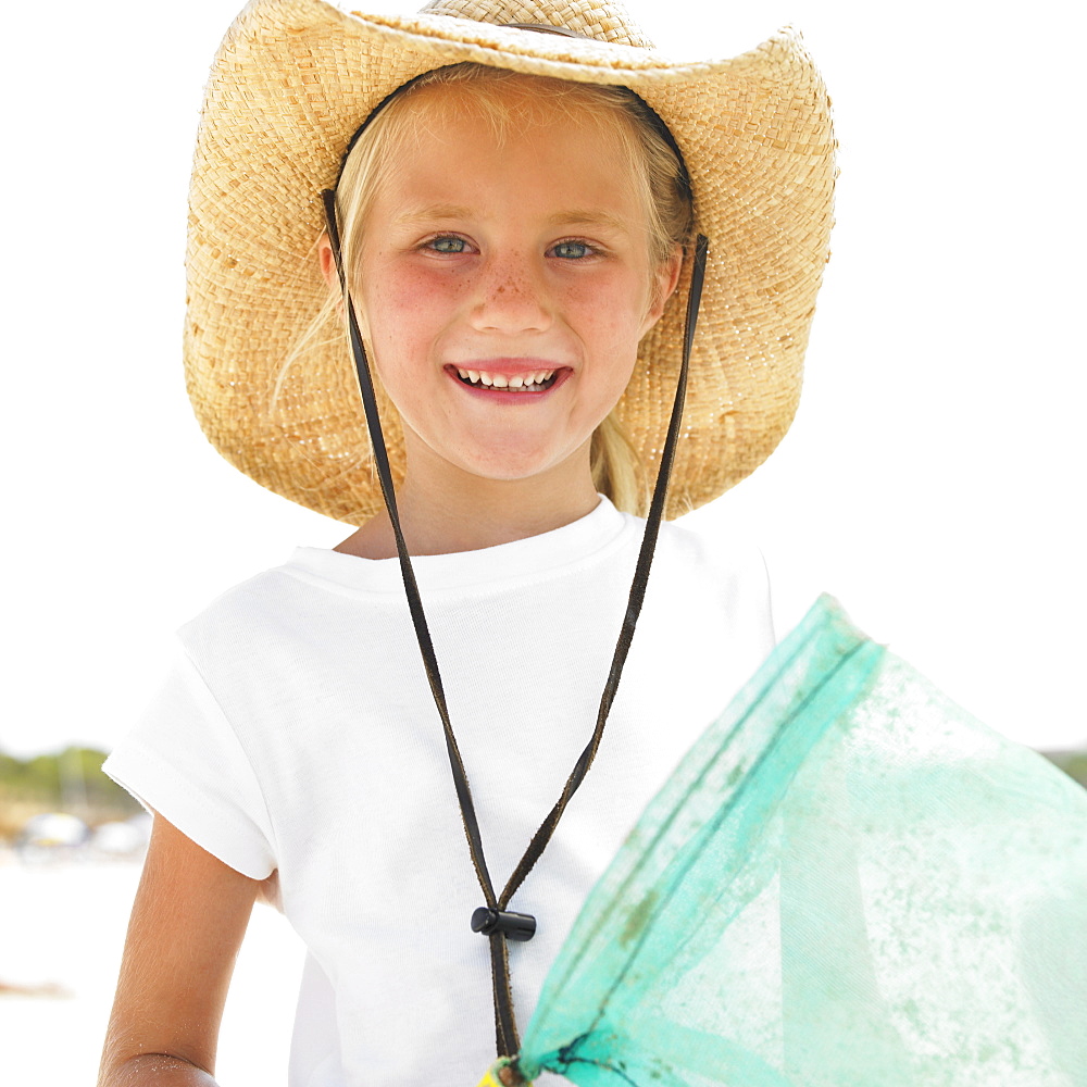 Girl (6-8) on beach wearing straw hat, carrying fishing pole