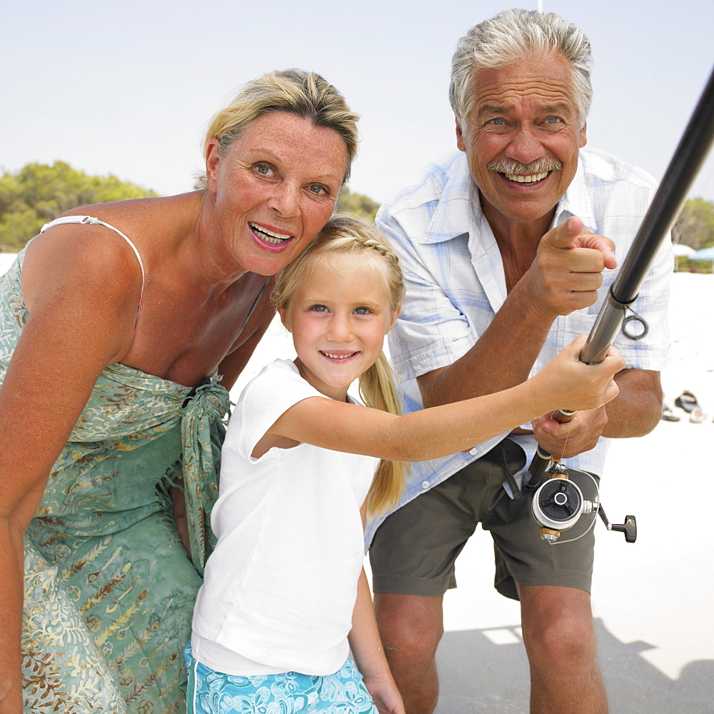 Grandparents and grandaughter (6-8) on beach holding fishing rod