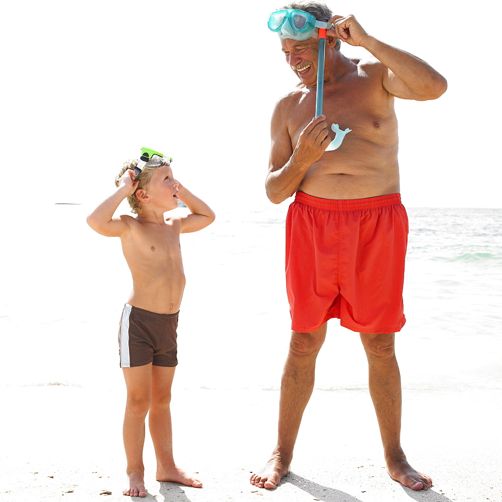 Grandfather and grandson (6-8) on beach with snorkelling masks