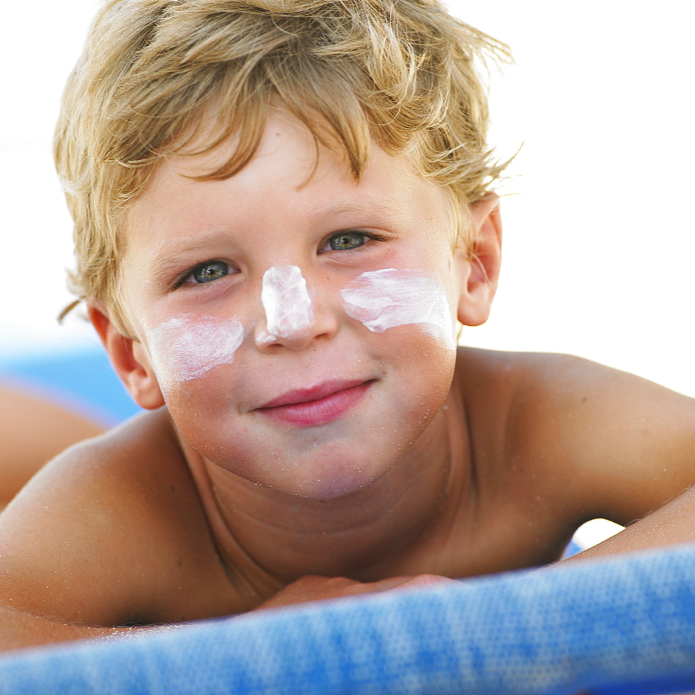 Boy (6-8) on beach with suncream on face