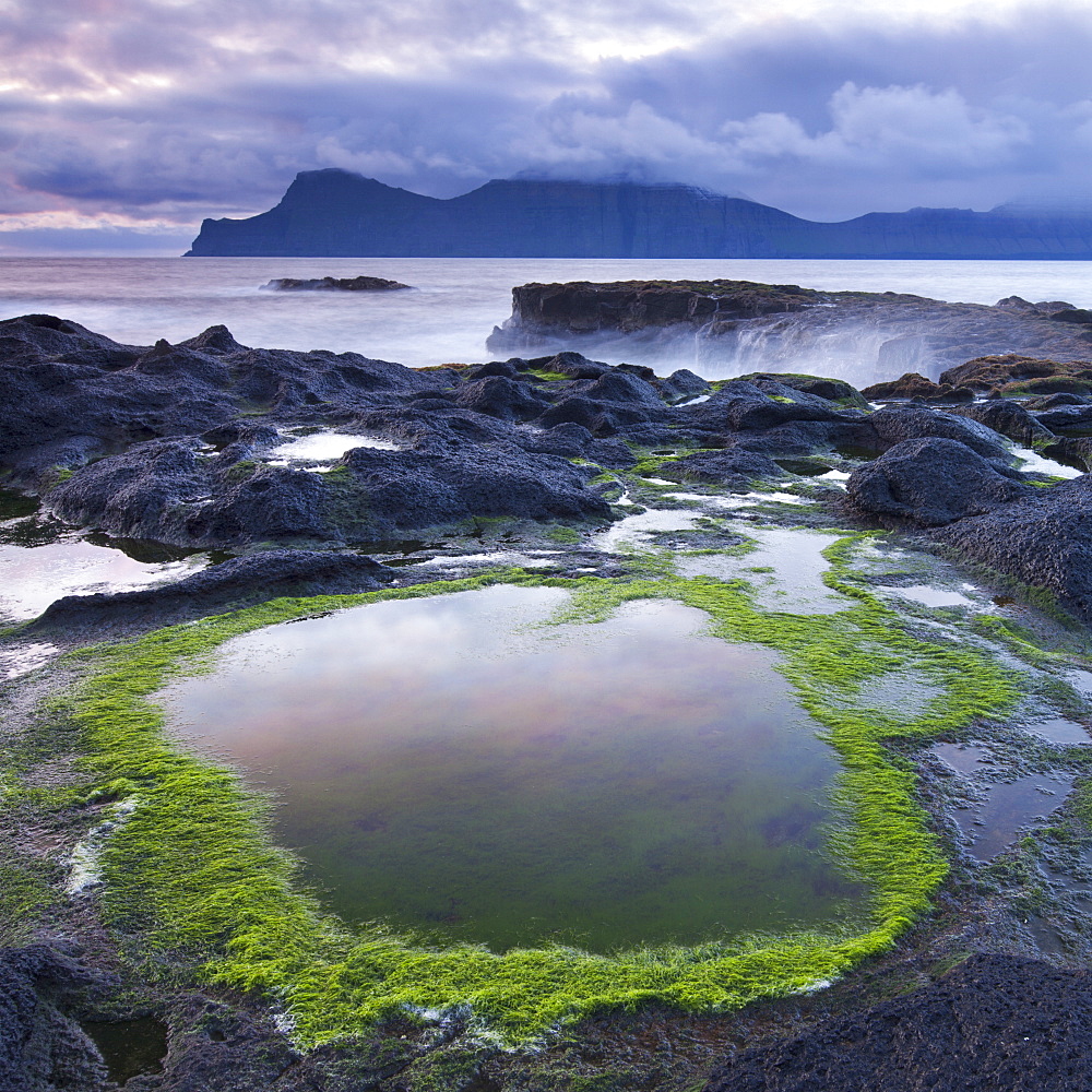 Rockpools on the shores of Gjogv on Eysturoy, looking towards the mountainous island of Kalsoy. Faroe Islands, Denmark, Europe