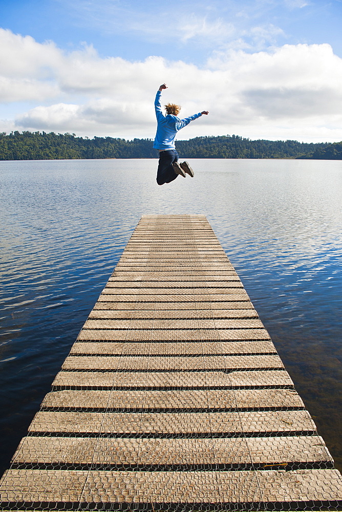 Woman jumping on a jetty at Lake Ianthe, West Coast, South Island, New Zealand, Pacific 