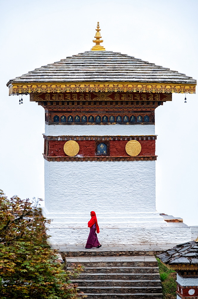 Single nun walking past temple at Dochula Pass, Bhutan, Asia