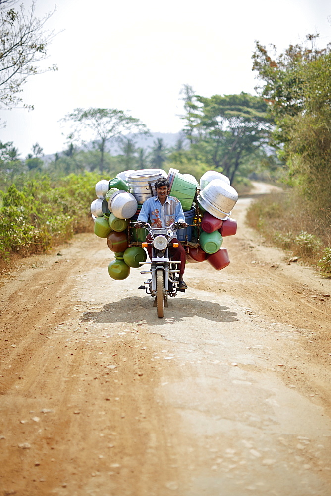 Peddler with water containers on a motorbike passing a road to Kabini, Karnataka, India