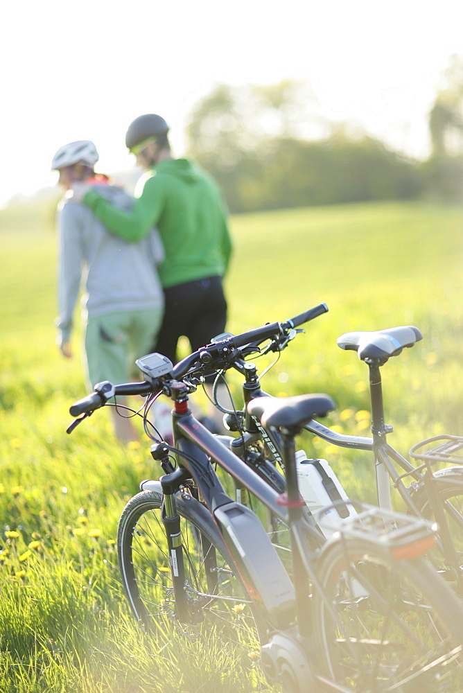 Two cyclists with E-bikes resting in a flower meadow, Munsing, Upper Bavaria, Germany
