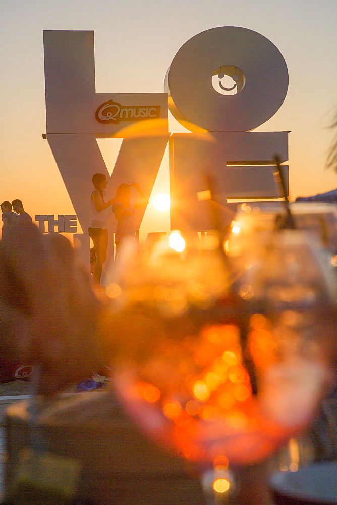 Love sculpture on the beach seen through a cocktail glass at sunset, Ostend, Flanders, Flemish Region, Belgium