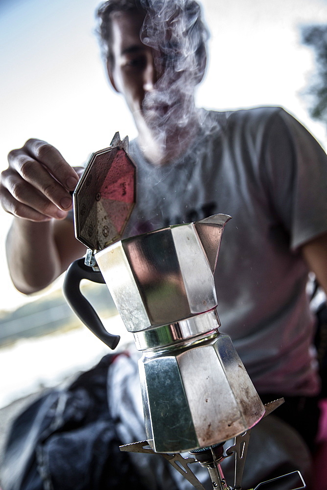 Young man making coffee with a camp cooker, Freilassing, Bavaria, Germany