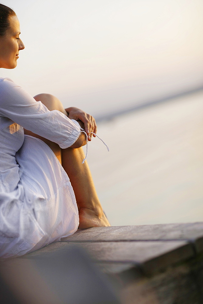 Woman sitting on jetty at lake Starnberg, Ambach, Bavaria, Germany