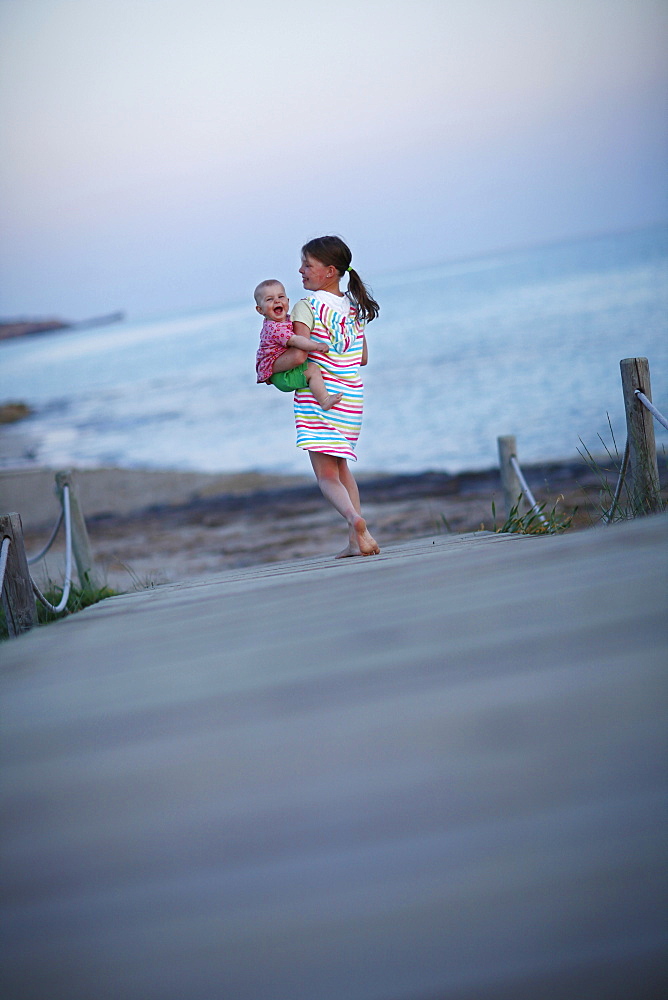 Girl carrying baby on jetty, Formentera, Balearic Islands, Spain