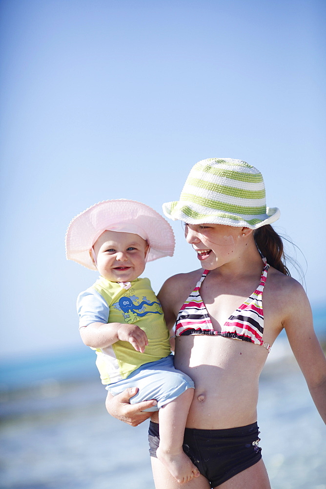 Girl carrying little sister on the beach, Es Arenals, Formentera, Balearic Islands, Spain