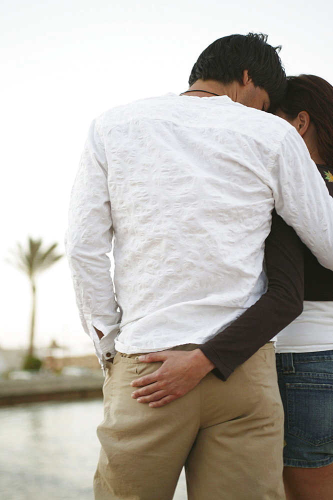 Couple in clothes hugging on the beach, rear view