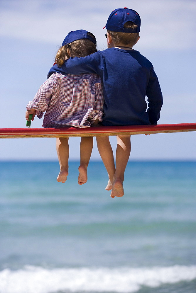 Two children sitting on bench before sea shore, boy hugging little girl, Apulia, Italy