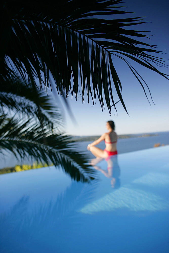 Woman sitting at edge of outdoor pool, sea in back, Bay of Porto Vecchio, Southern Corse, Frankreich