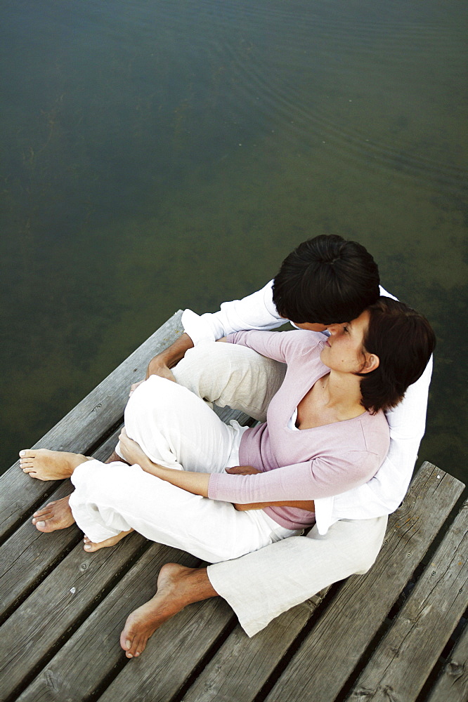 Couple sitting on jetty, man with arms around woman