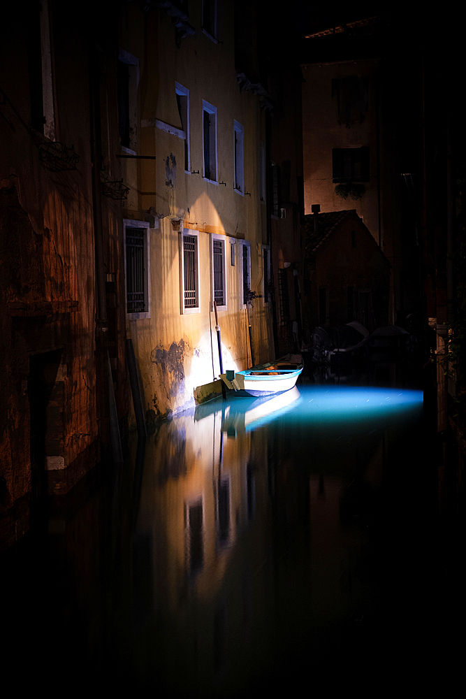 View of a lighted boat and fish in a canal in San Marco at night, Venice, Veneto, Italy, Europe